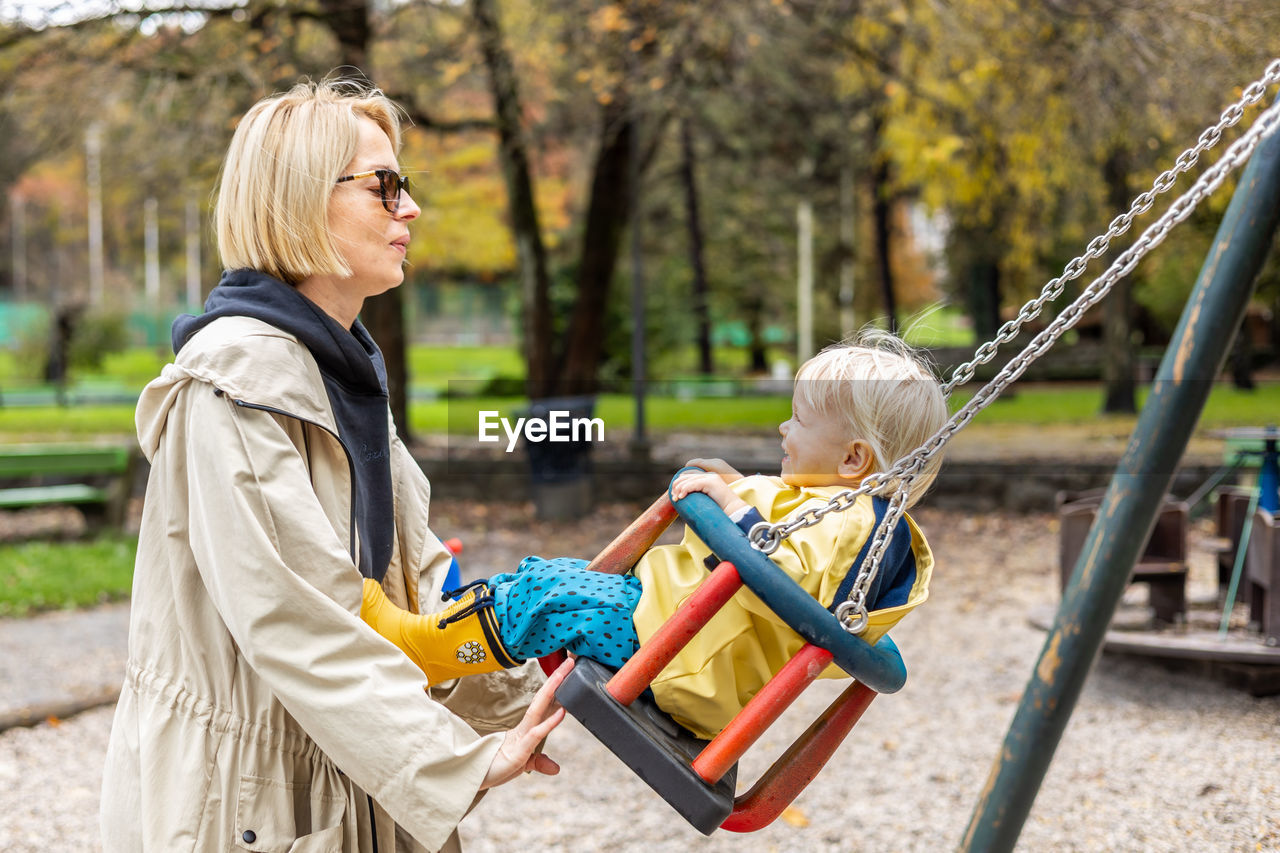 portrait of smiling young woman sitting on swing at playground