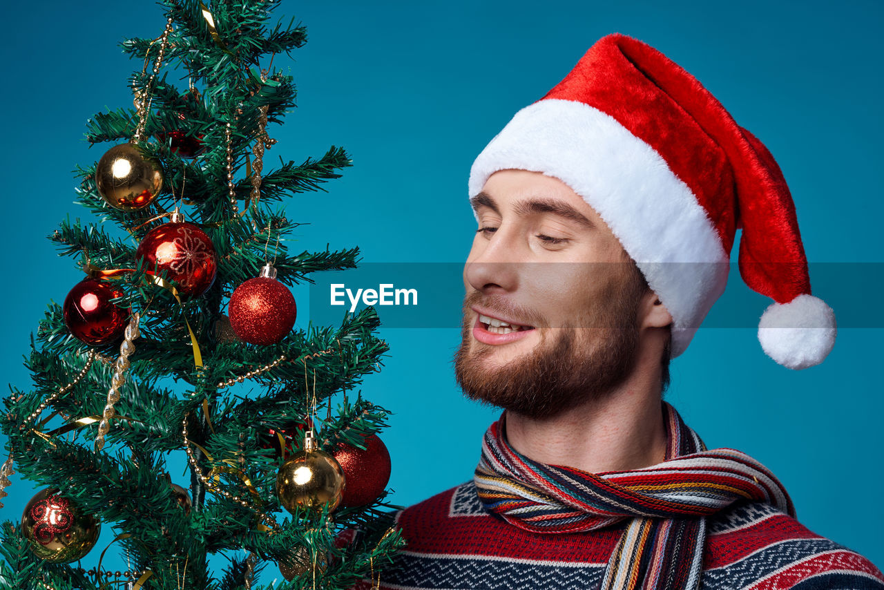 PORTRAIT OF SMILING YOUNG MAN WITH CHRISTMAS TREE AGAINST SKY