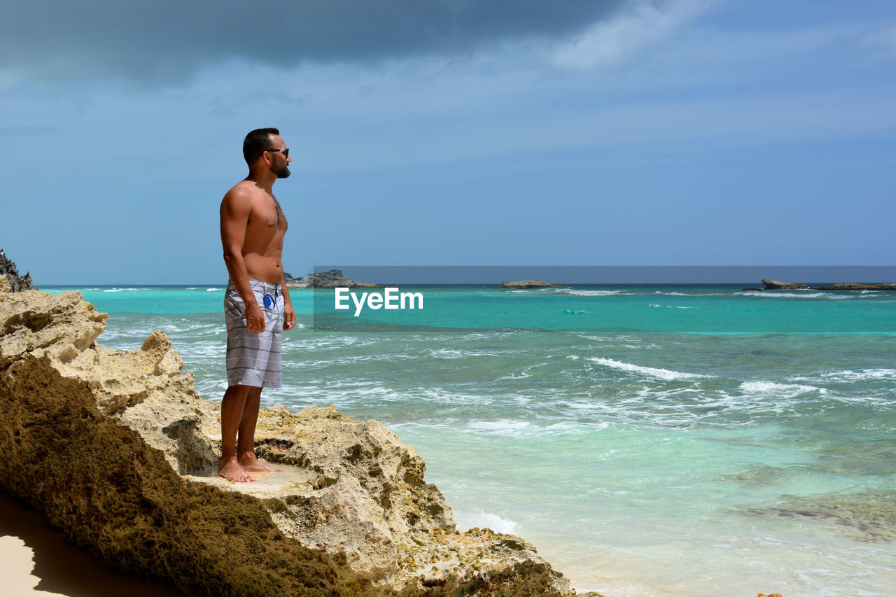 Man standing on rock at beach against sky