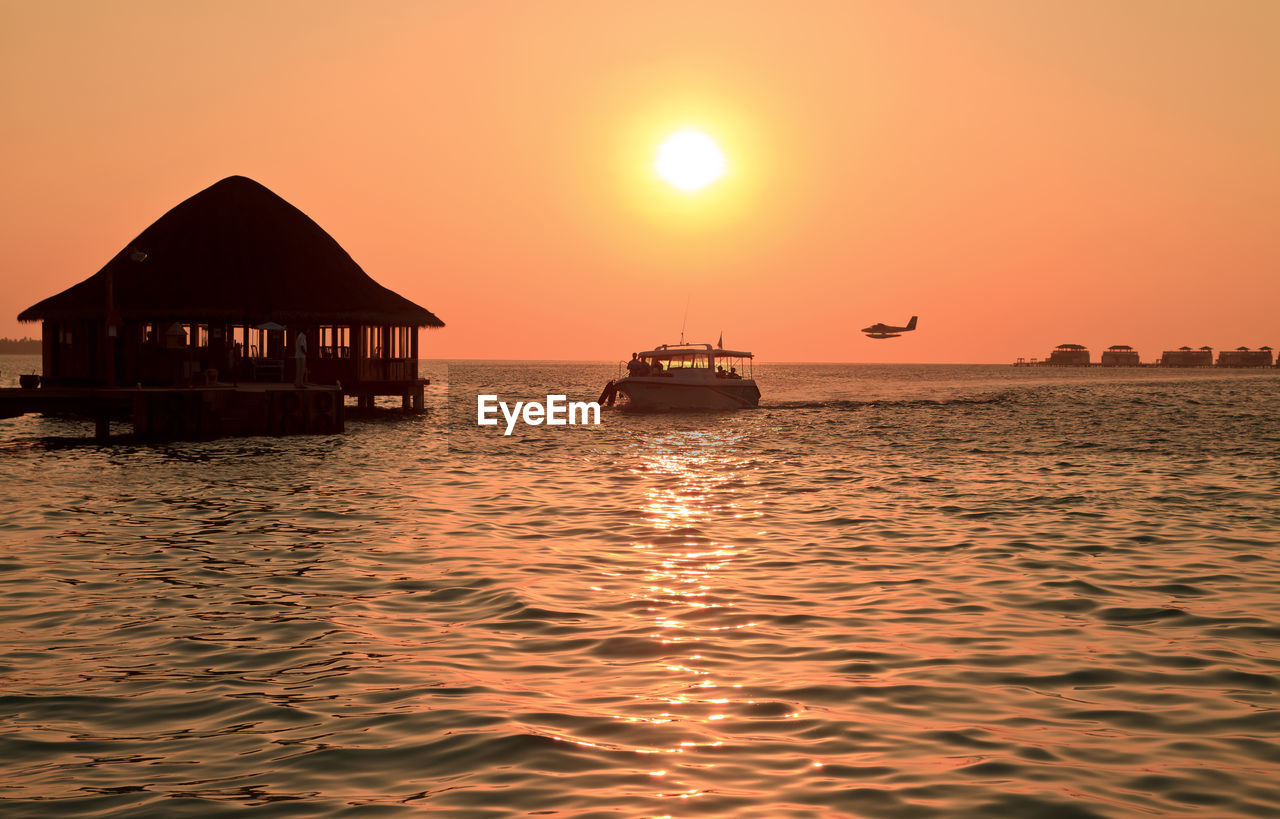 Silhouette of boat, boat house, and plane in sea