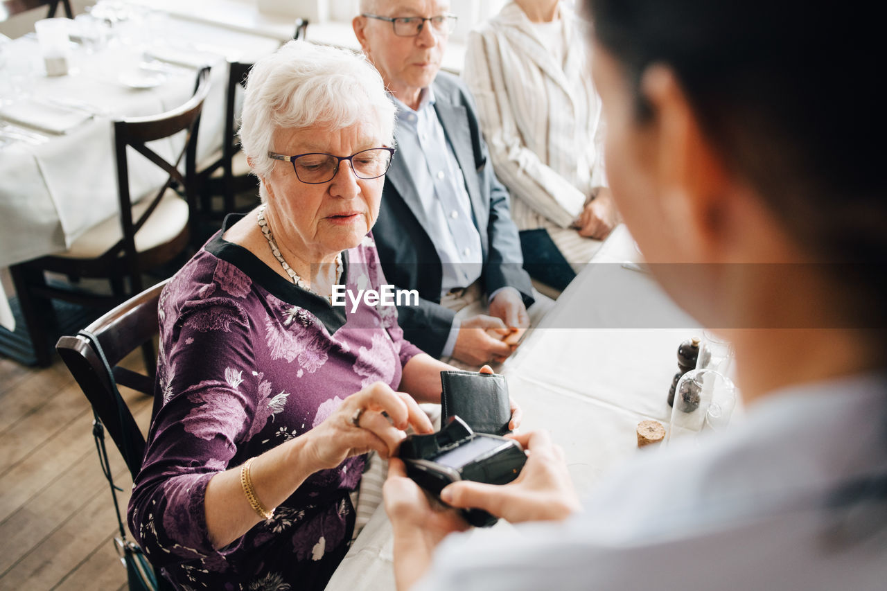 High angle view of owner holding credit card reader while senior woman paying in restaurant