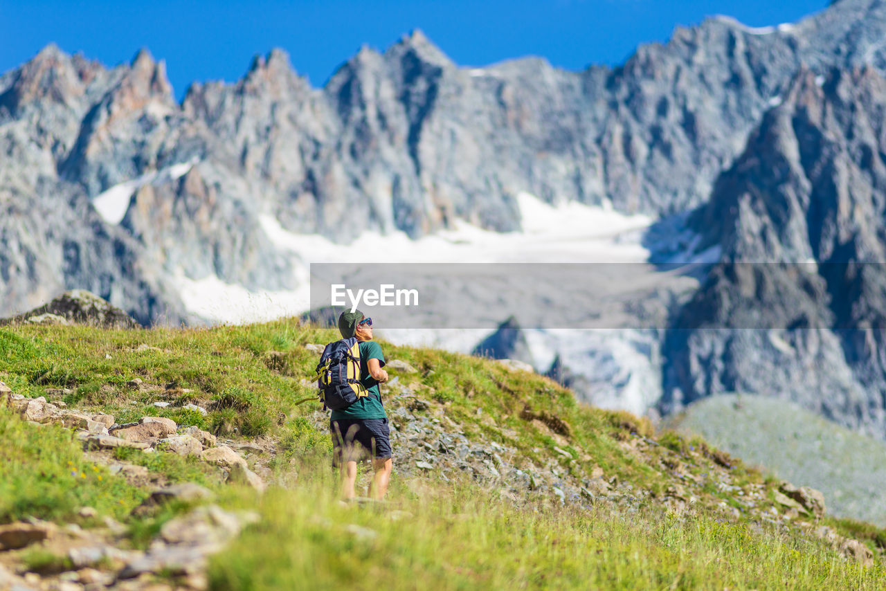 REAR VIEW OF PEOPLE ON MOUNTAIN AGAINST MOUNTAINS