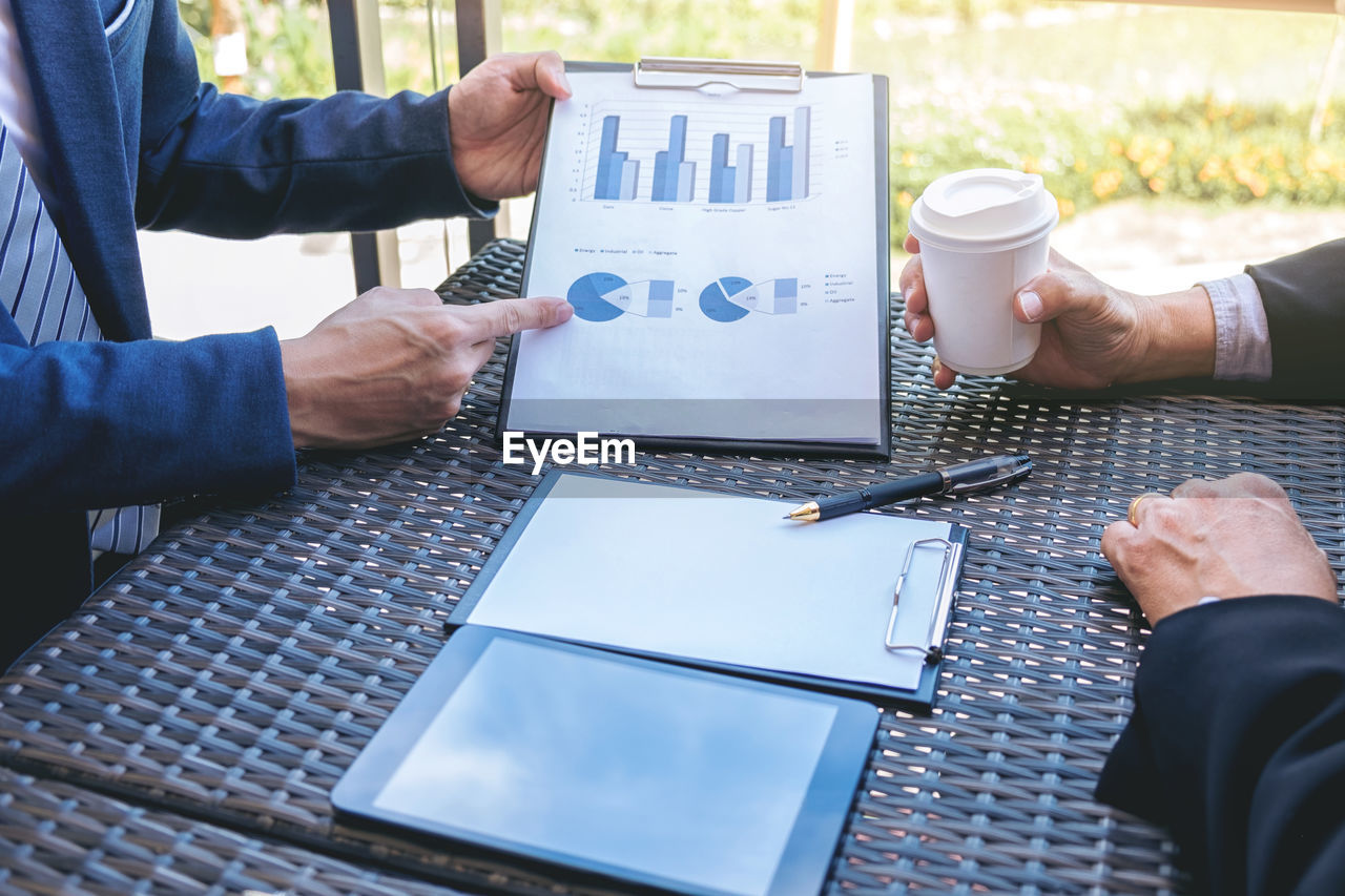 Midsection of businessmen discussing over graph at desk