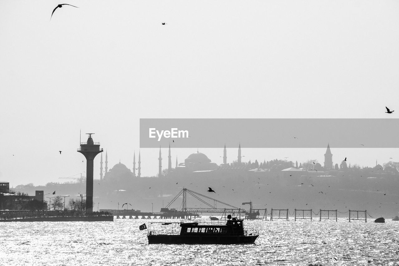 Silhouette boat sailing in straits by mosque against clear sky