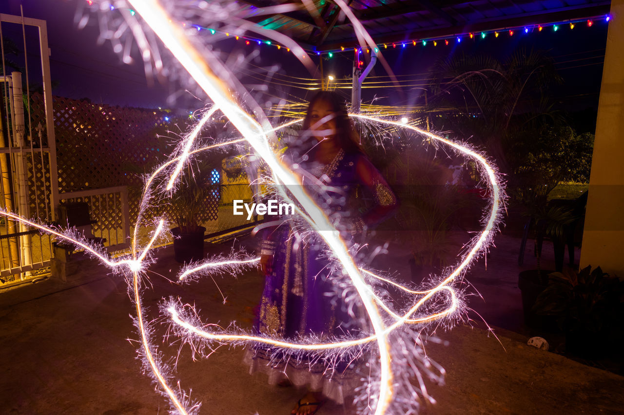 Young woman standing amidst firework display at night