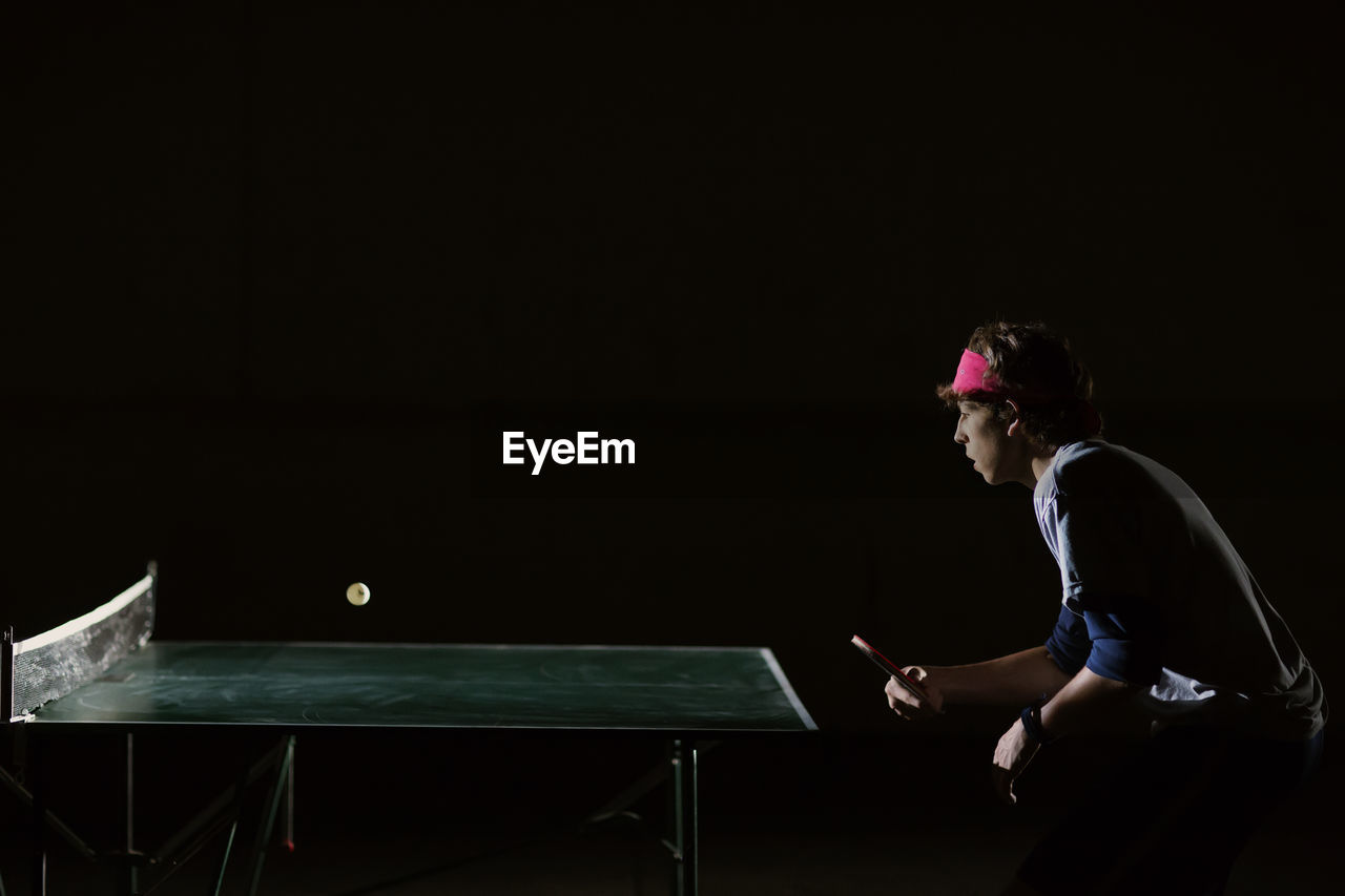 Man playing table tennis against black background