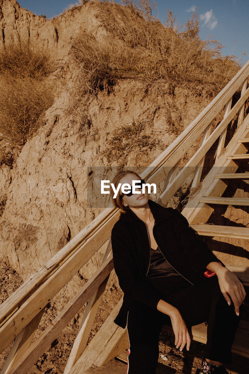 Woman wearing sunglasses while sitting on staircase against mountain