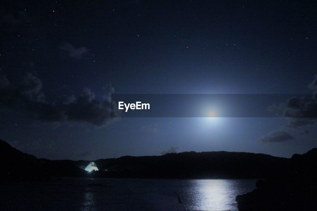 SILHOUETTE MOUNTAIN BY SEA AGAINST SKY AT NIGHT