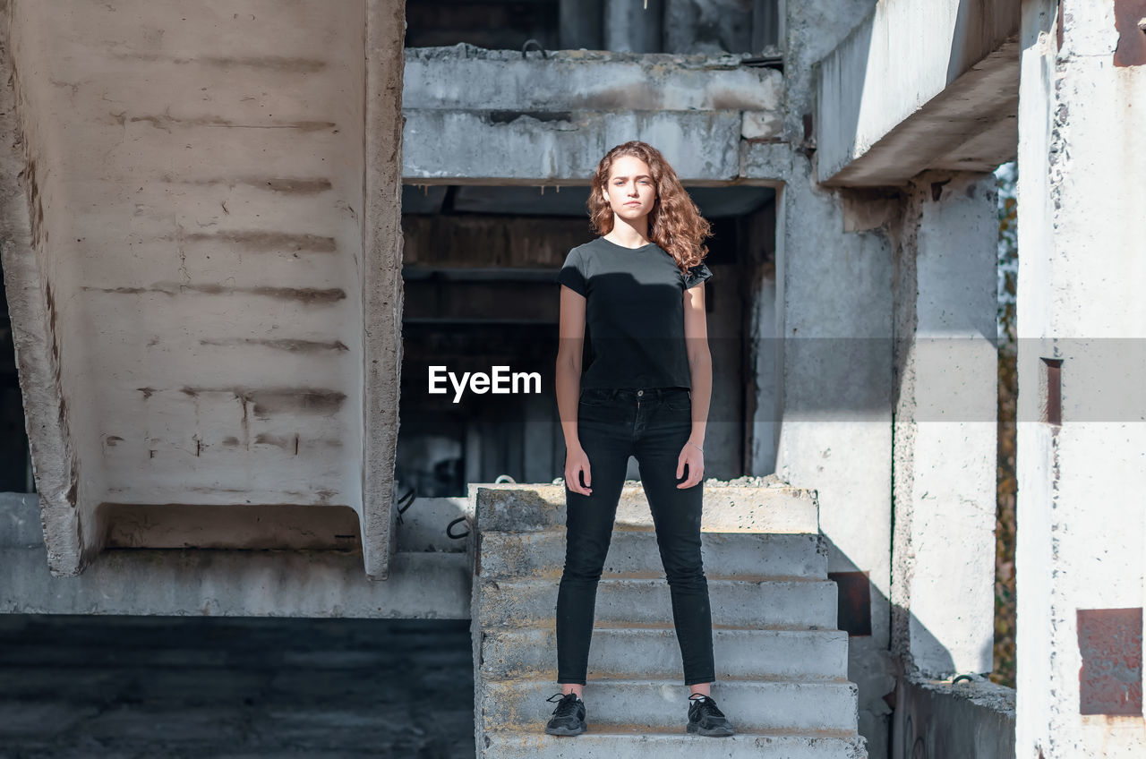 Cute teenage girl with curly hair standing on stairs. abandoned building, unfinished construction.