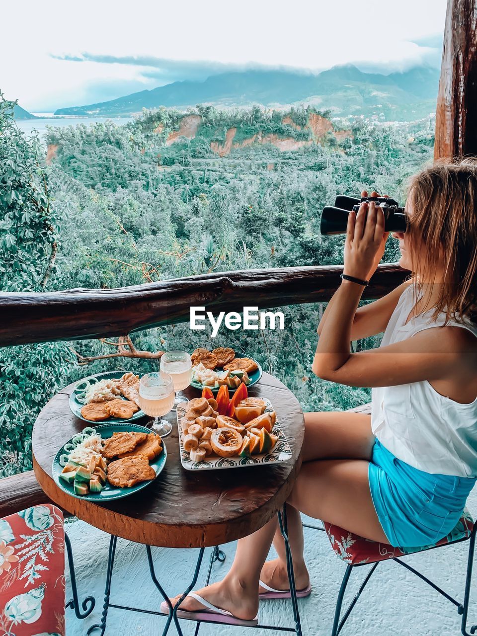 Woman using binoculars while sitting by food on table