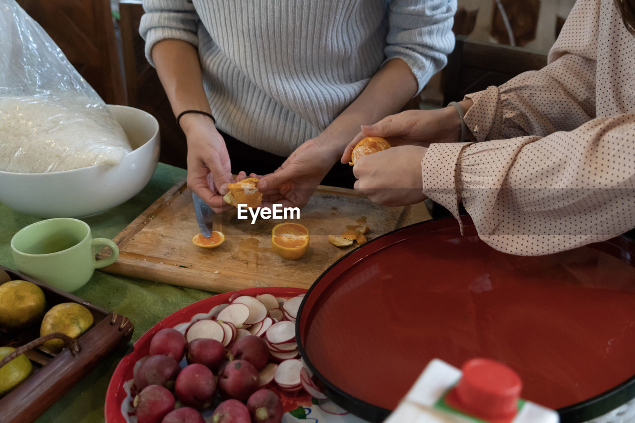 Midsection of women peeling of orange fruits