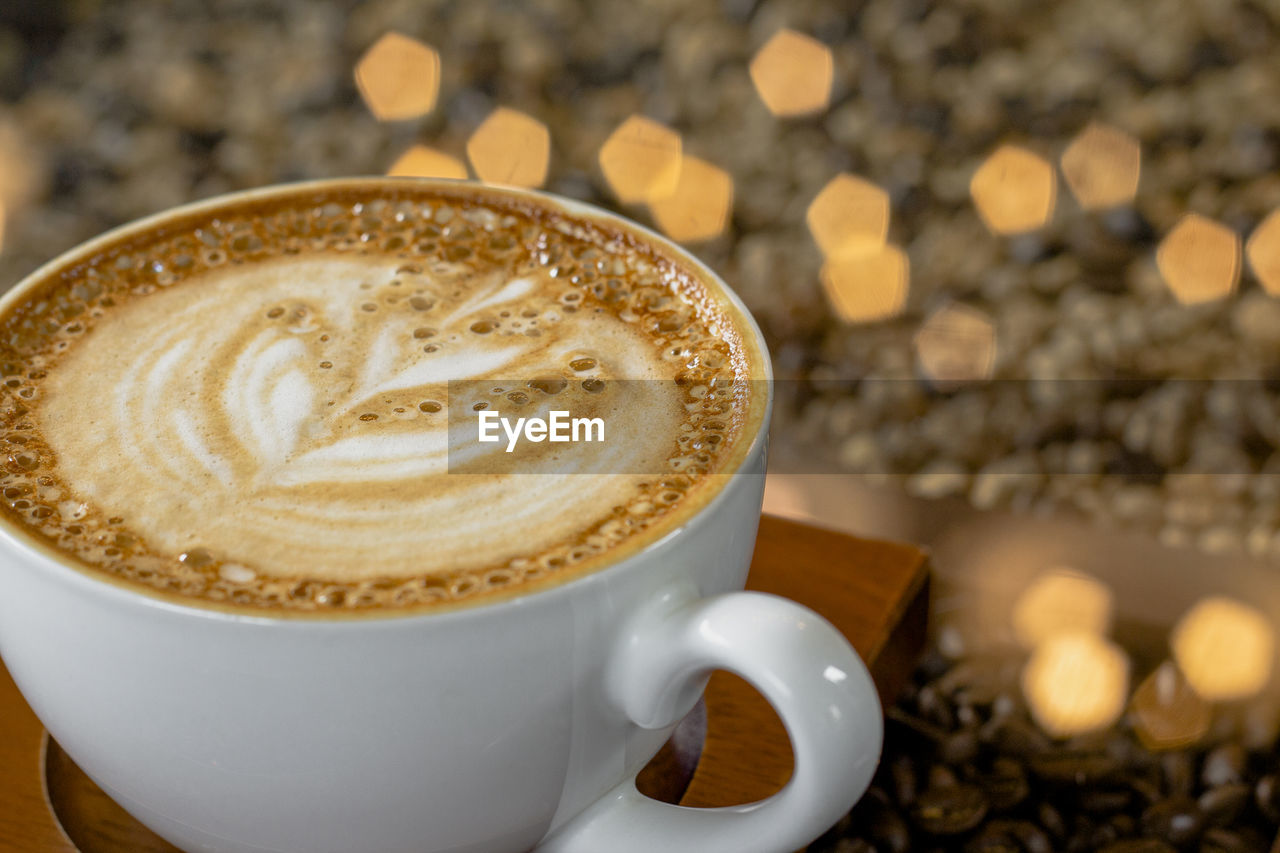 Latte art coffee with bokeh of lights on table, dark tone