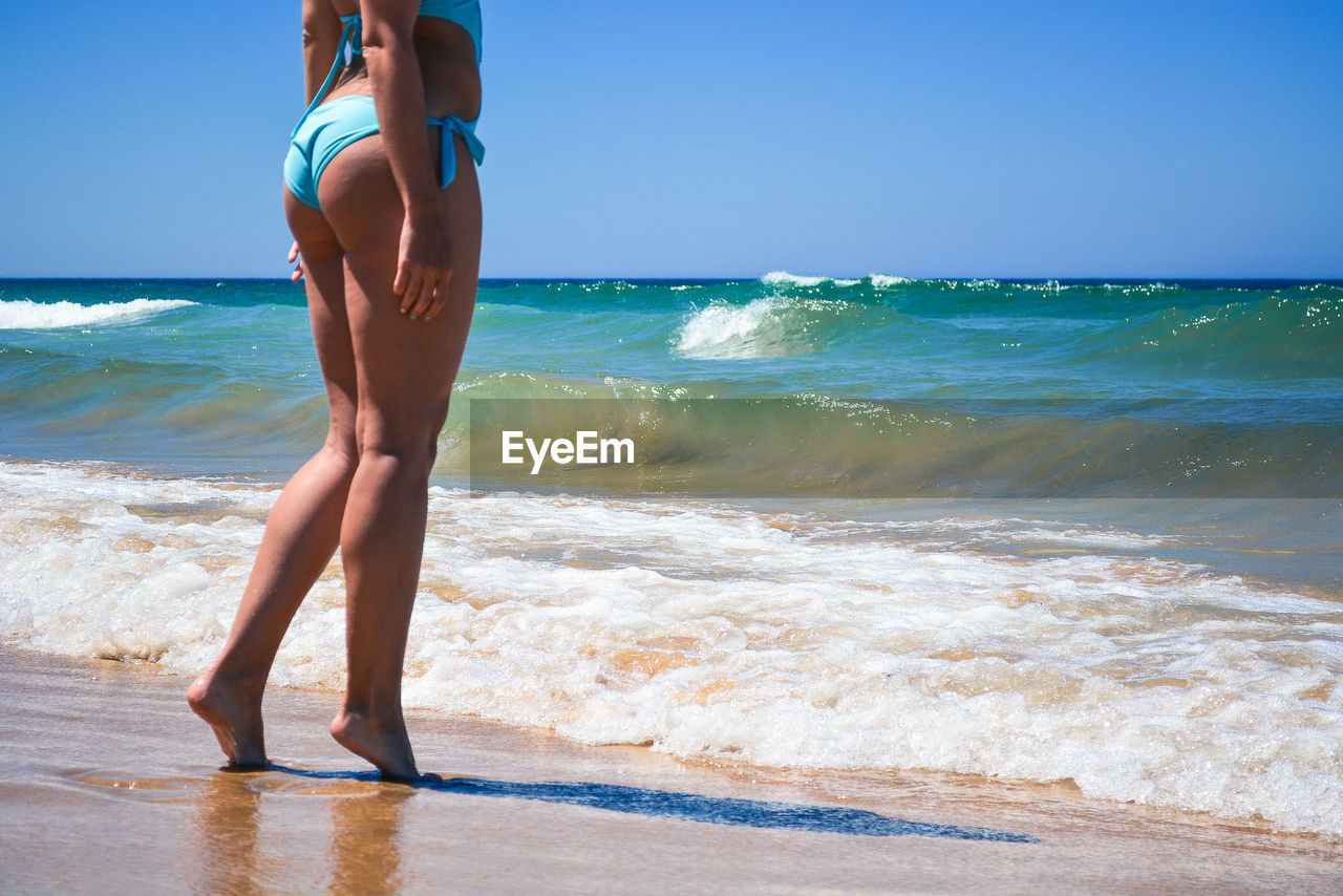 Low section of woman wearing bikini while standing on shore at beach