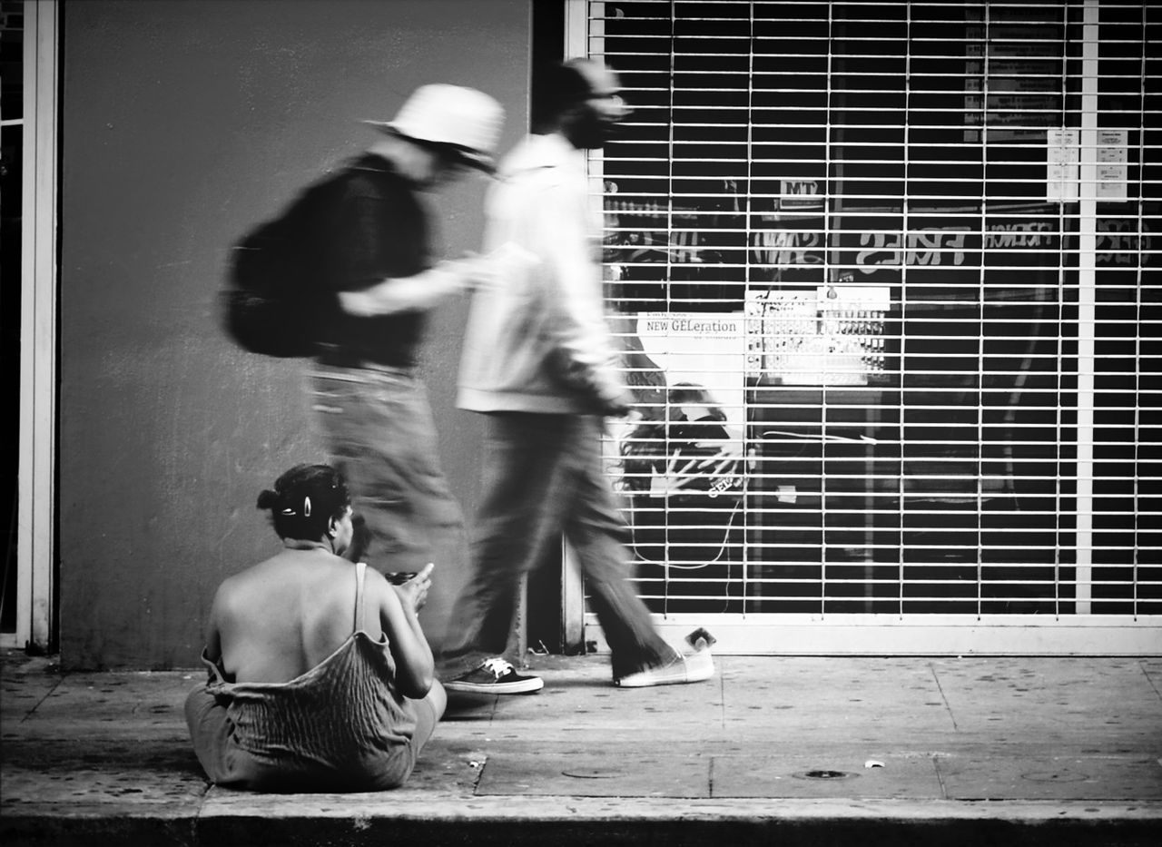 Blurred motion of men walking by beggar on sidewalk
