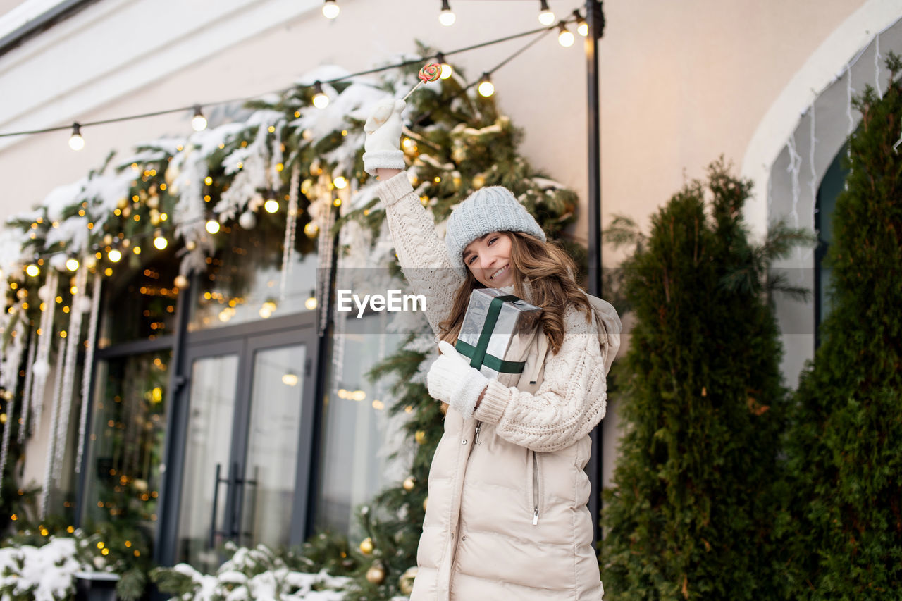 plant, adult, women, clothing, one person, smiling, happiness, hat, nature, celebration, christmas, winter, emotion, standing, female, warm clothing, lifestyles, tree, portrait, holiday, christmas tree, decoration, spring, front view, flower, cheerful, outdoors, young adult, holding, day, three quarter length, architecture, floristry, leisure activity, looking, waist up, business finance and industry, flowering plant, enjoyment