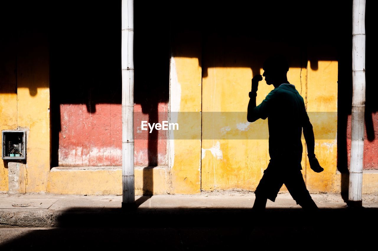 Silhouette man walking on street against colourful building