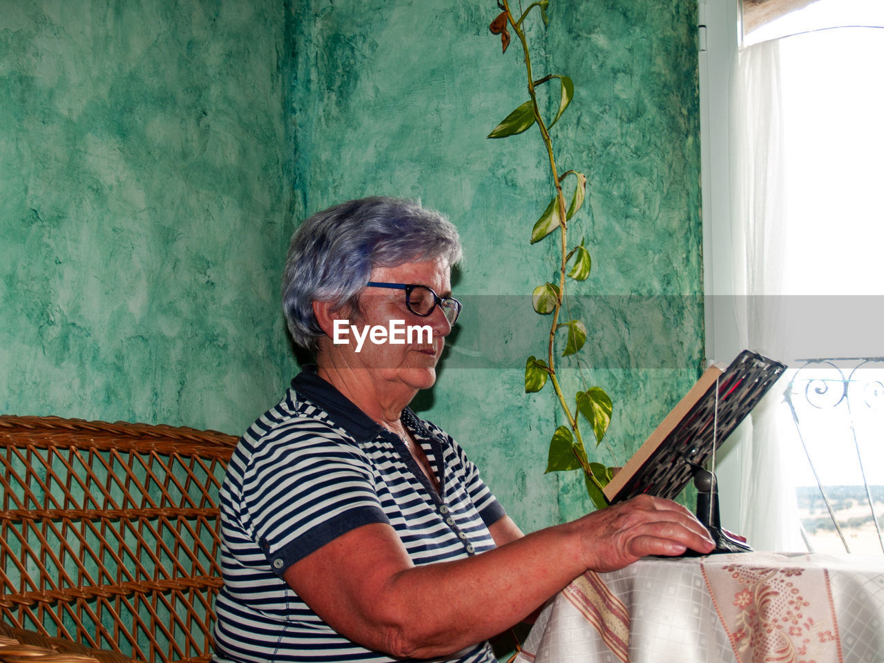 Woman reading book while sitting by window at home