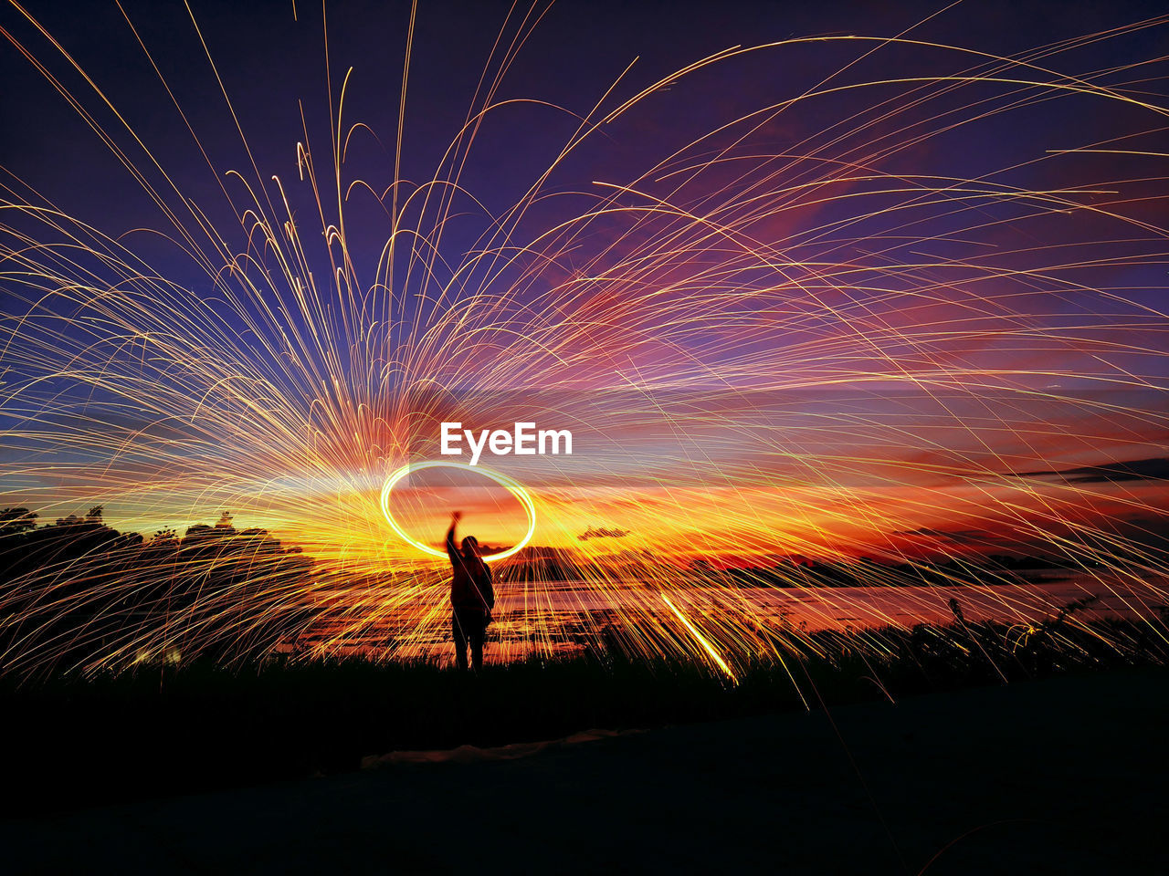 Silhouette man spinning wire wool at beach against sky during sunset