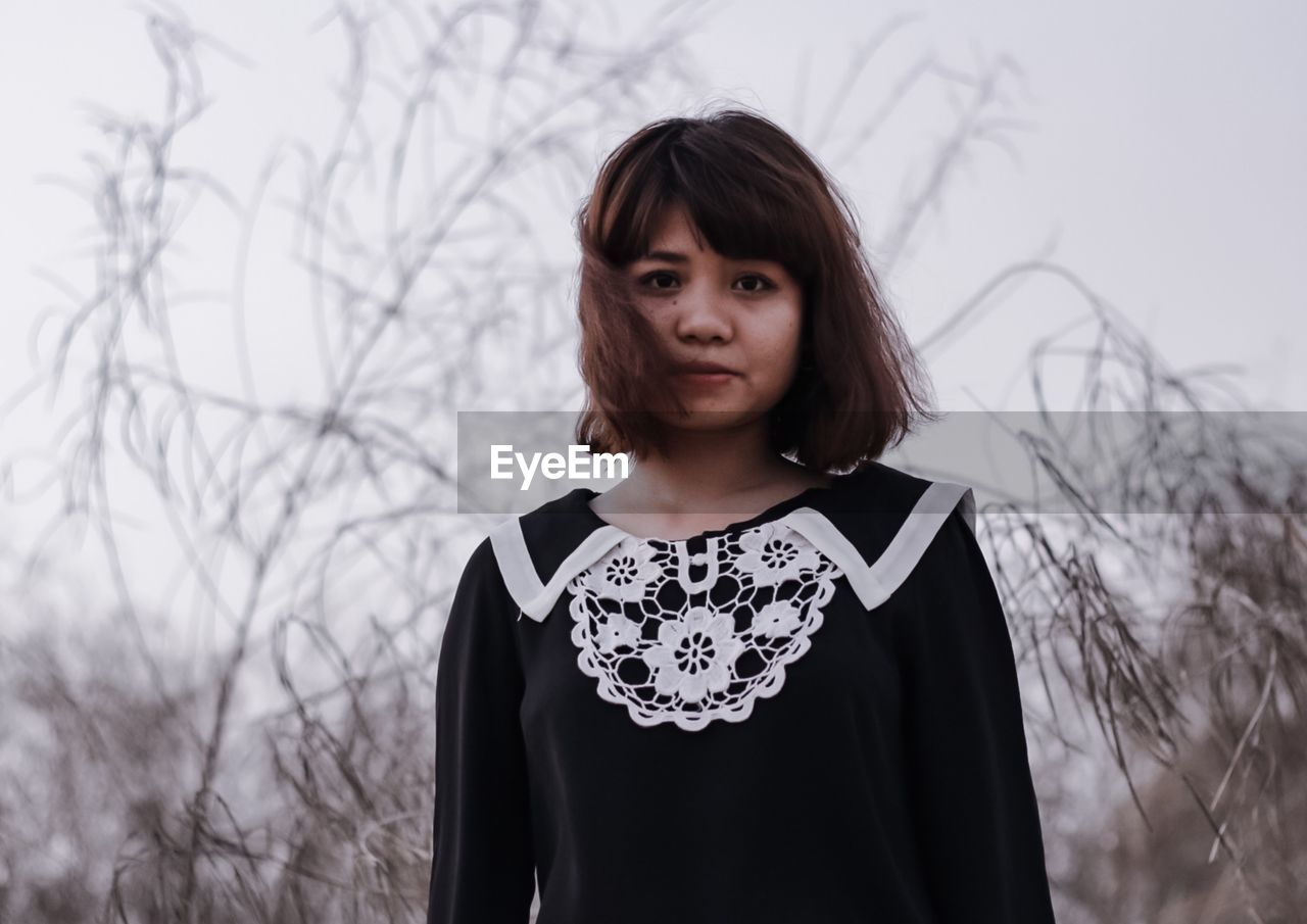 Portrait of young woman standing against bare tree