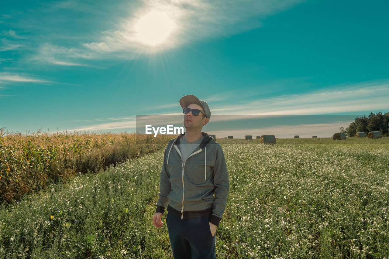 Portrait of young man standing on field against sky