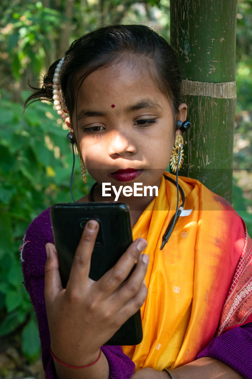 A tribal little girl is listening to music with bluetooth headphones on her android phone