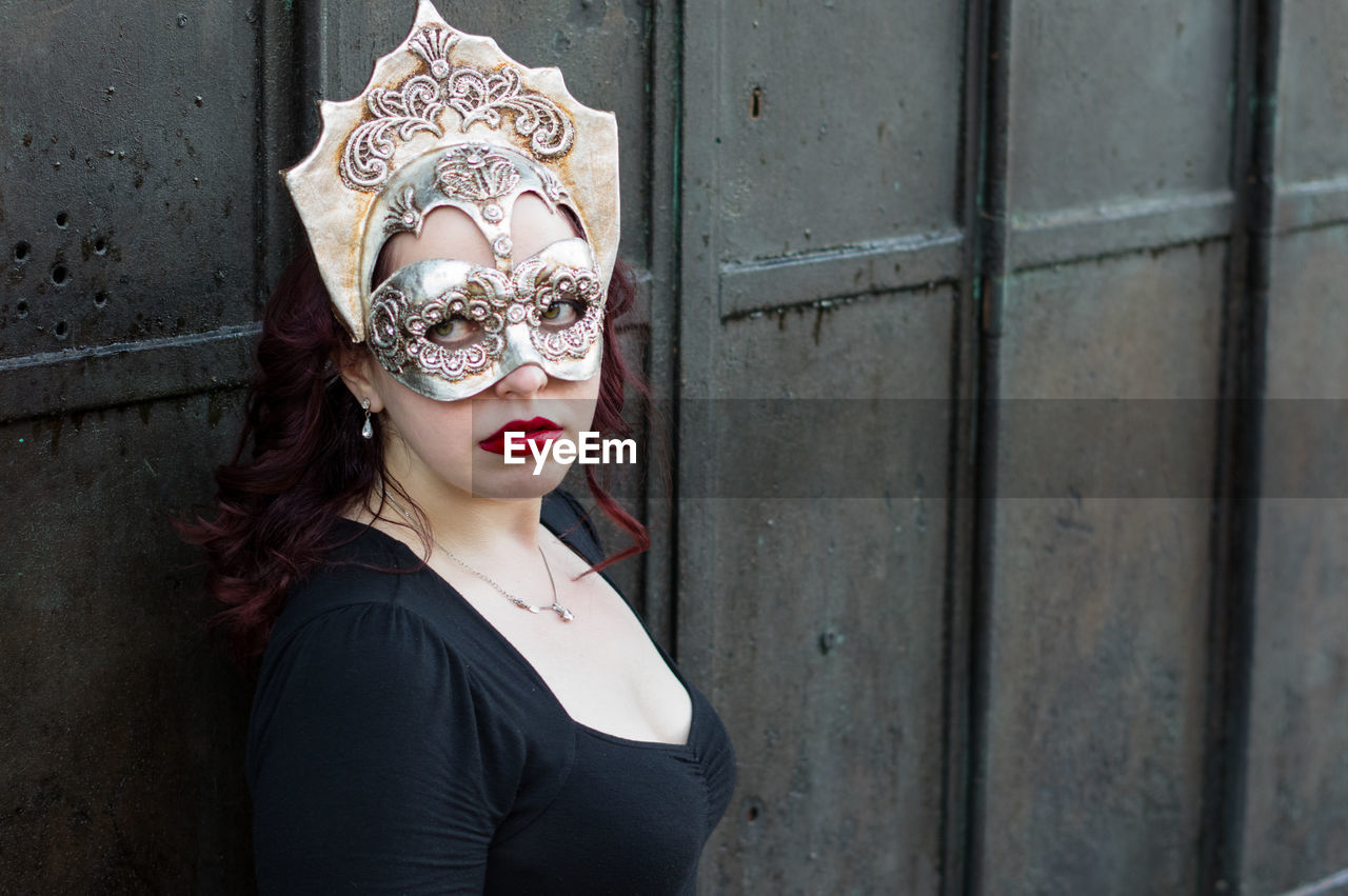 Close-up of woman wearing venetian mask against wall