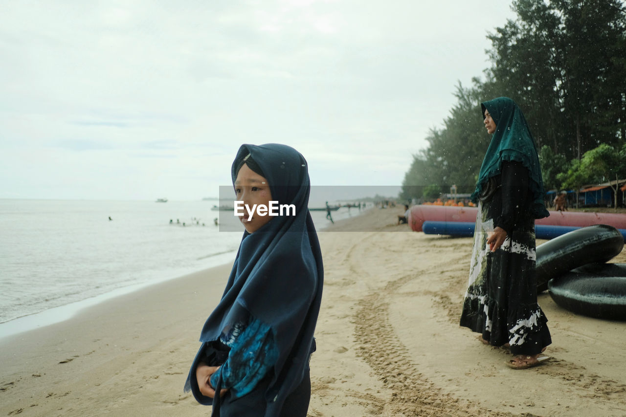 FRIENDS STANDING ON BEACH AGAINST SEA