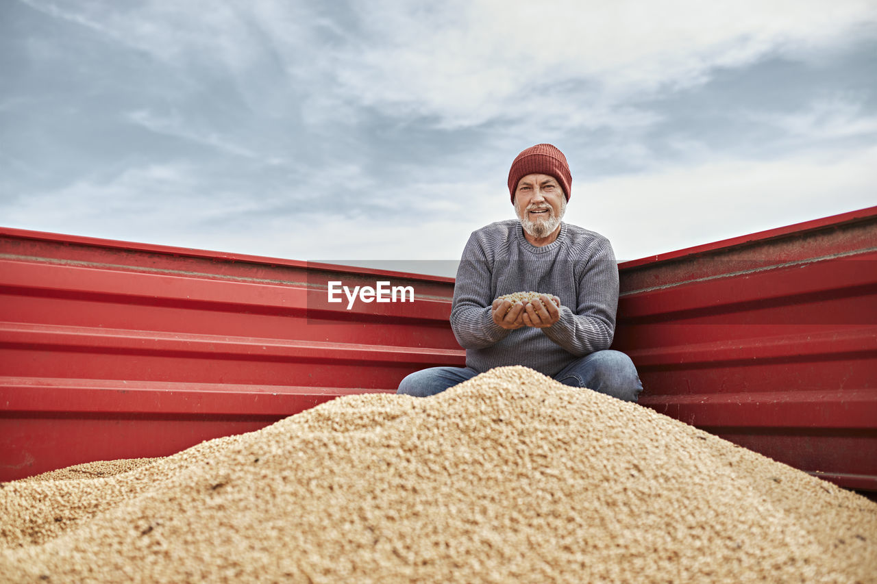 Smiling farmer examining soybean while sitting in tractor against clear sky