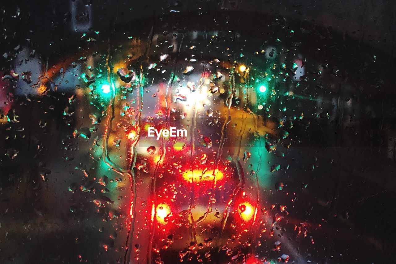 Illuminated lights seen through wet glass window of car at night