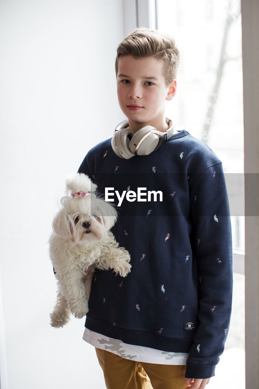 PORTRAIT OF BOY WITH DOG STANDING AGAINST WHITE WALL