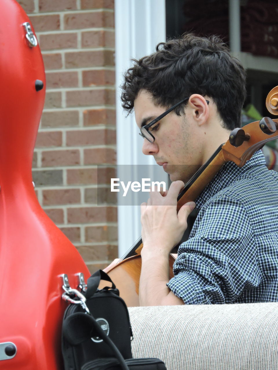 Side view of man playing cello against building