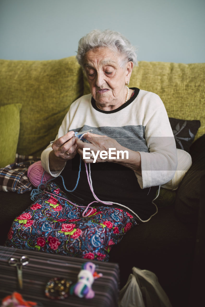 Portrait of crocheting senior woman sitting on couch at home