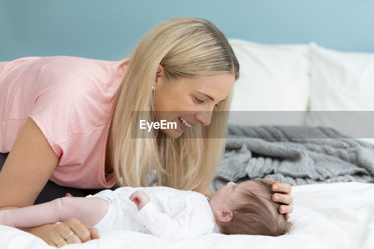 Mother playing with baby girl on bed at home