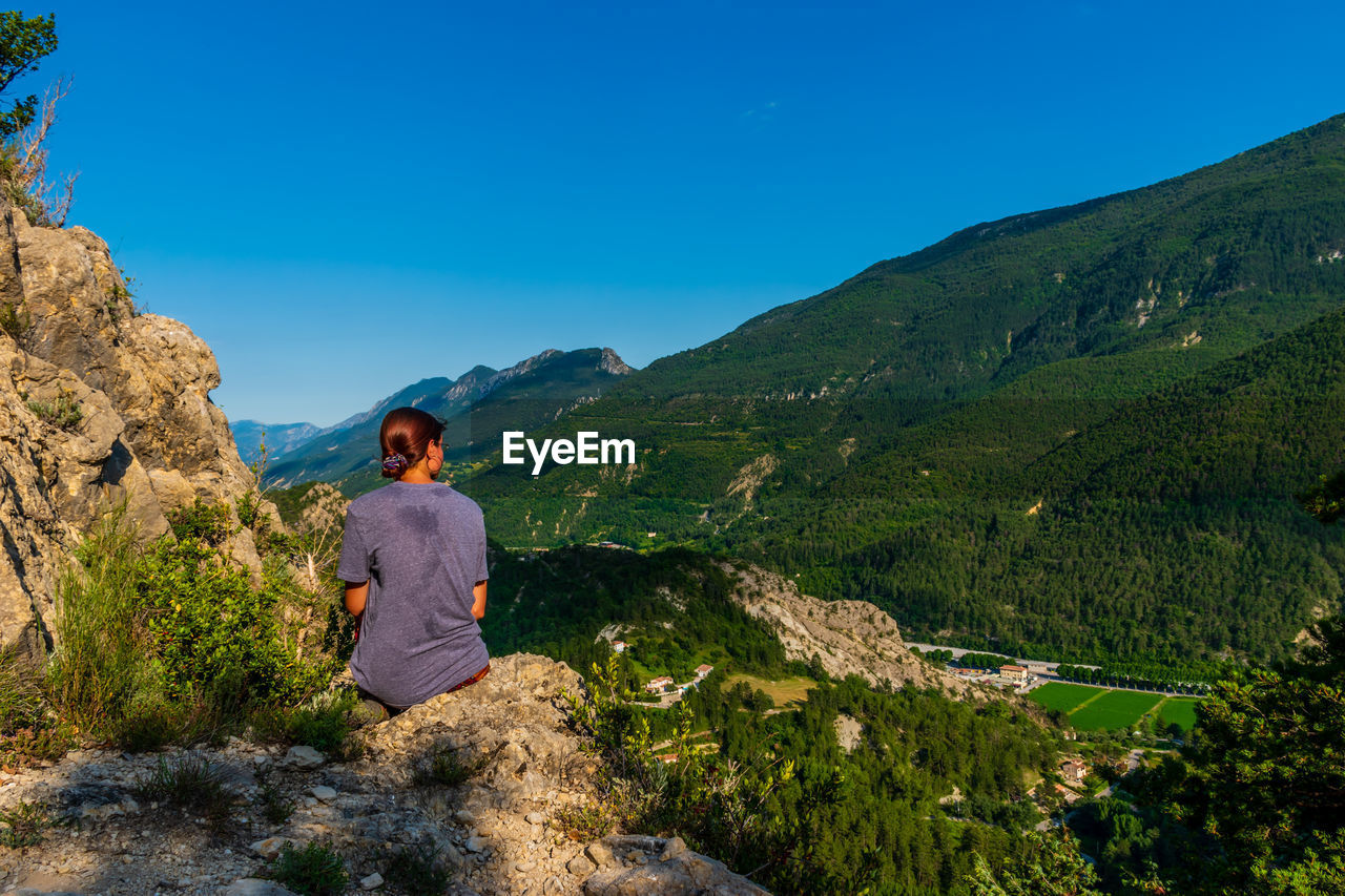 Rear view of man looking at mountains against blue sky