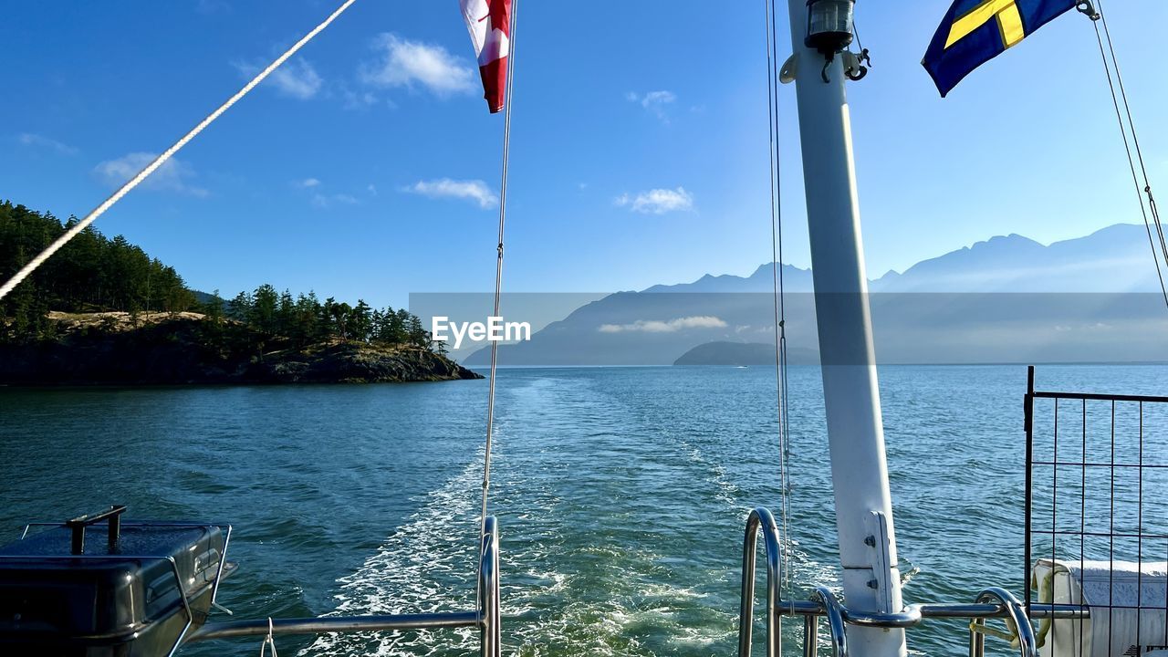 water, sky, flag, sea, nature, nautical vessel, transportation, sailing, environment, scenics - nature, patriotism, travel, no people, mountain, beauty in nature, ship, vehicle, blue, mode of transportation, day, travel destinations, tranquility, outdoors, tranquil scene, boat, pole, cloud, wind, land, vacation, mast, sailboat, holiday, trip, sunlight, ocean, summer, idyllic, tree, tourism