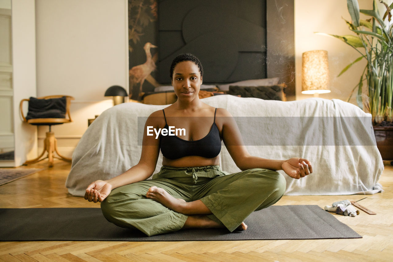 Portrait of smiling young woman exercising on mat in bedroom at home