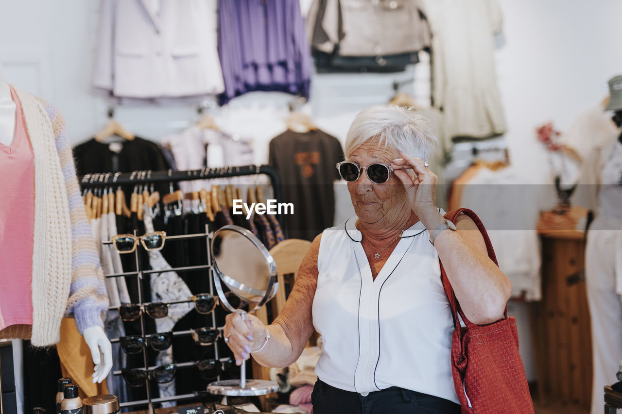 Senior woman in clothes shop trying sunglasses