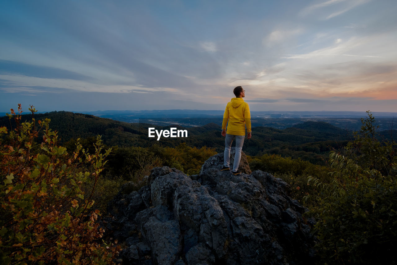 Rear view of man standing on rock against sky