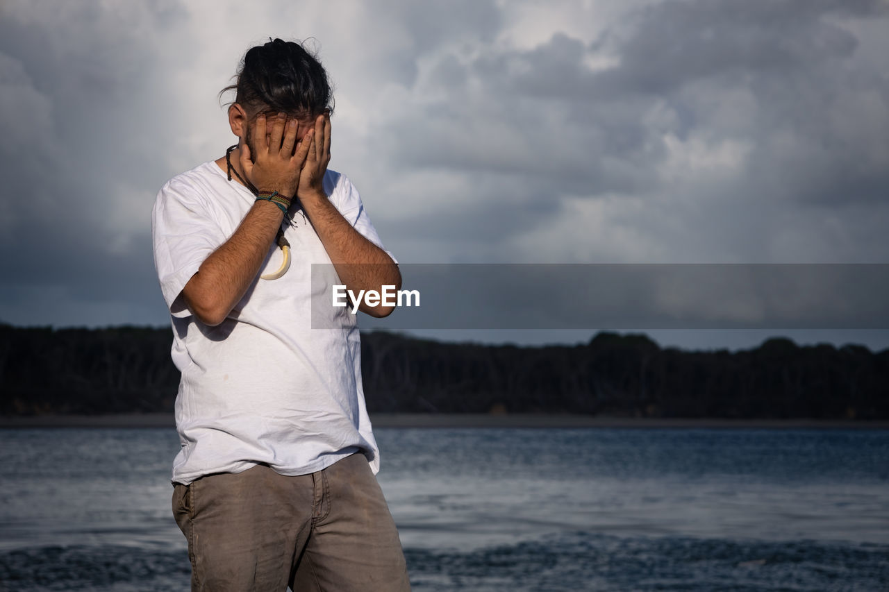 Side view of young man drinking water while standing against lake