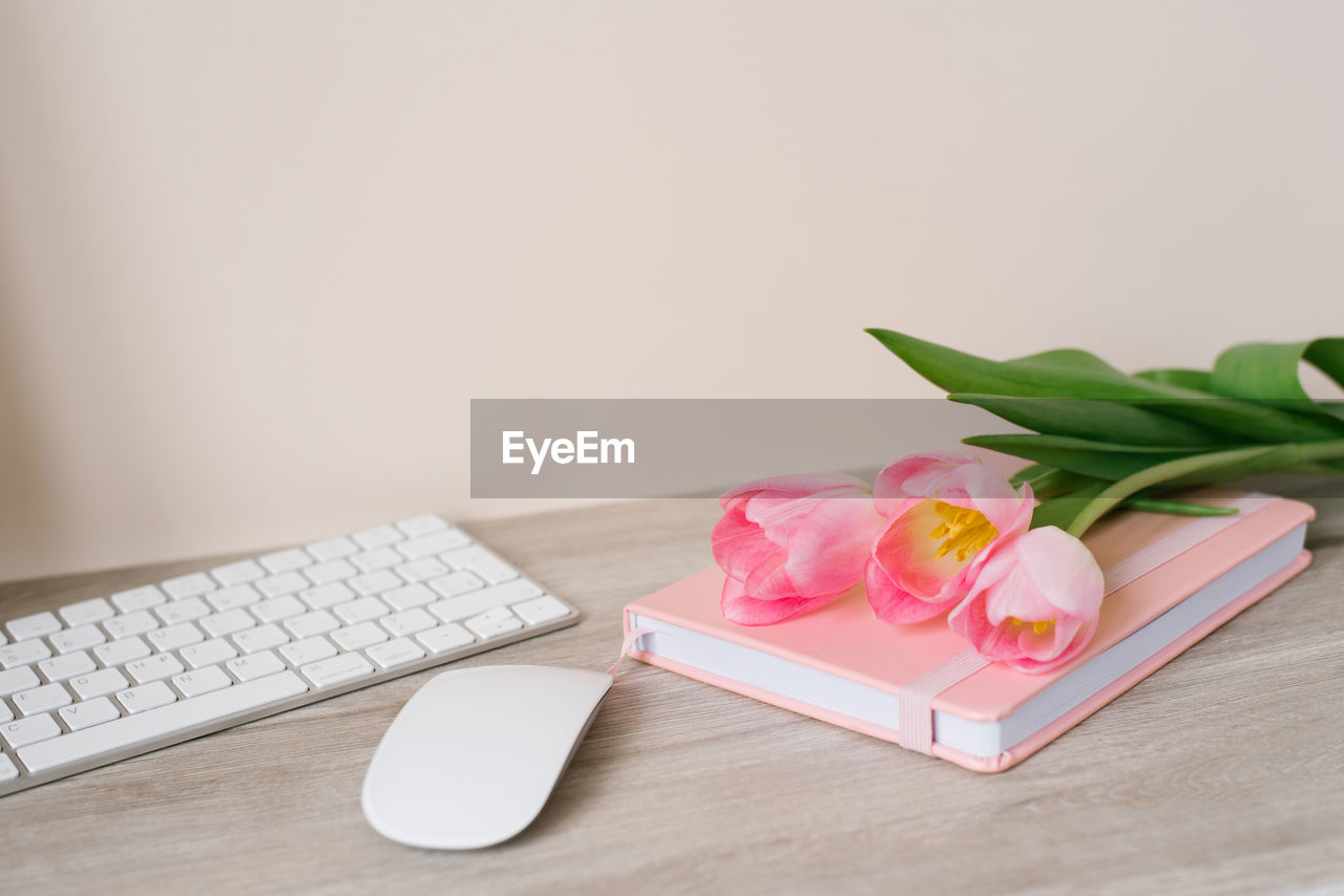 Workspace with keyboard, pink diary and pink tulips on wooden background. space for text