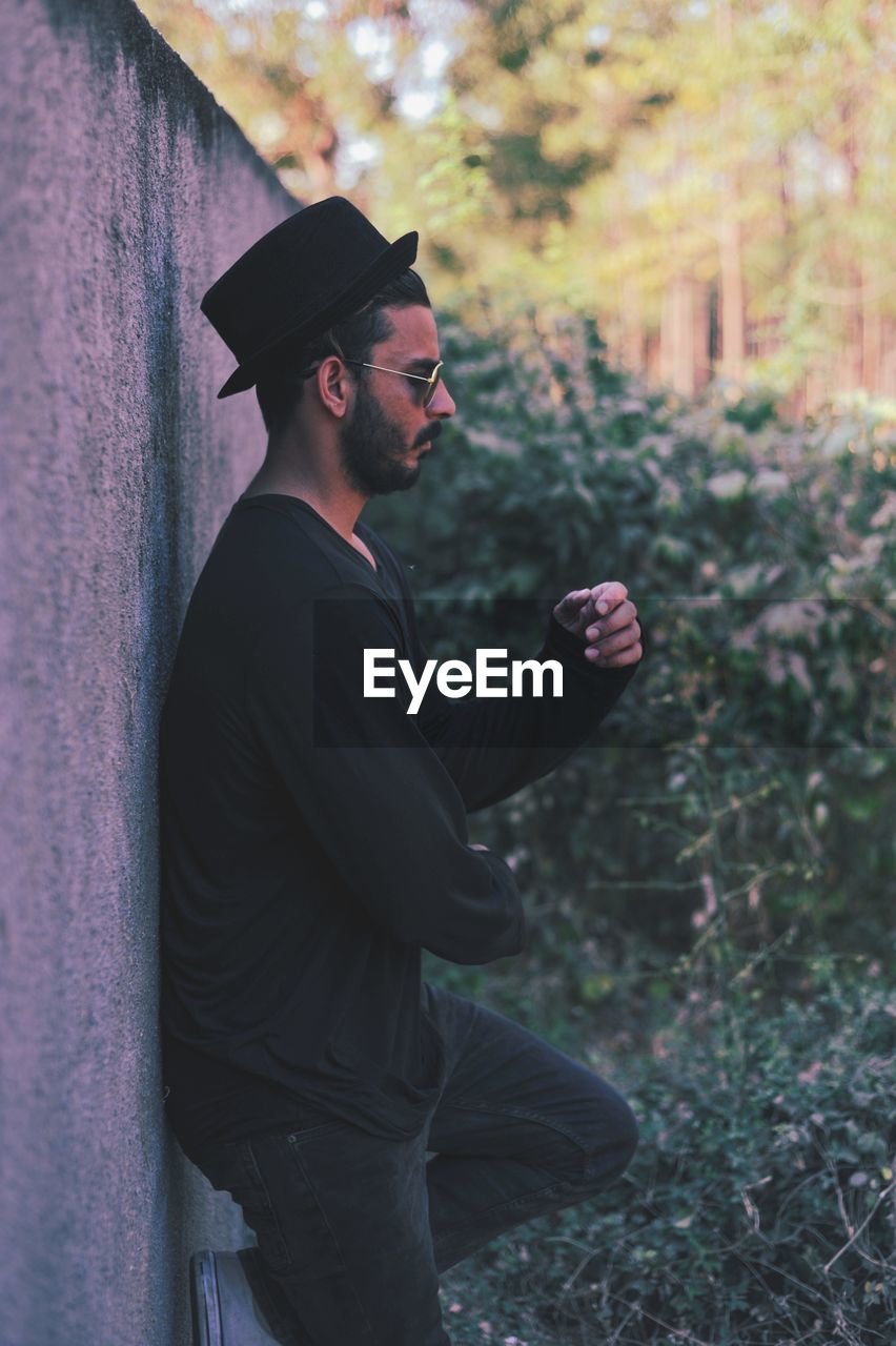 SIDE VIEW OF YOUNG MAN LOOKING AWAY WHILE STANDING OUTDOORS