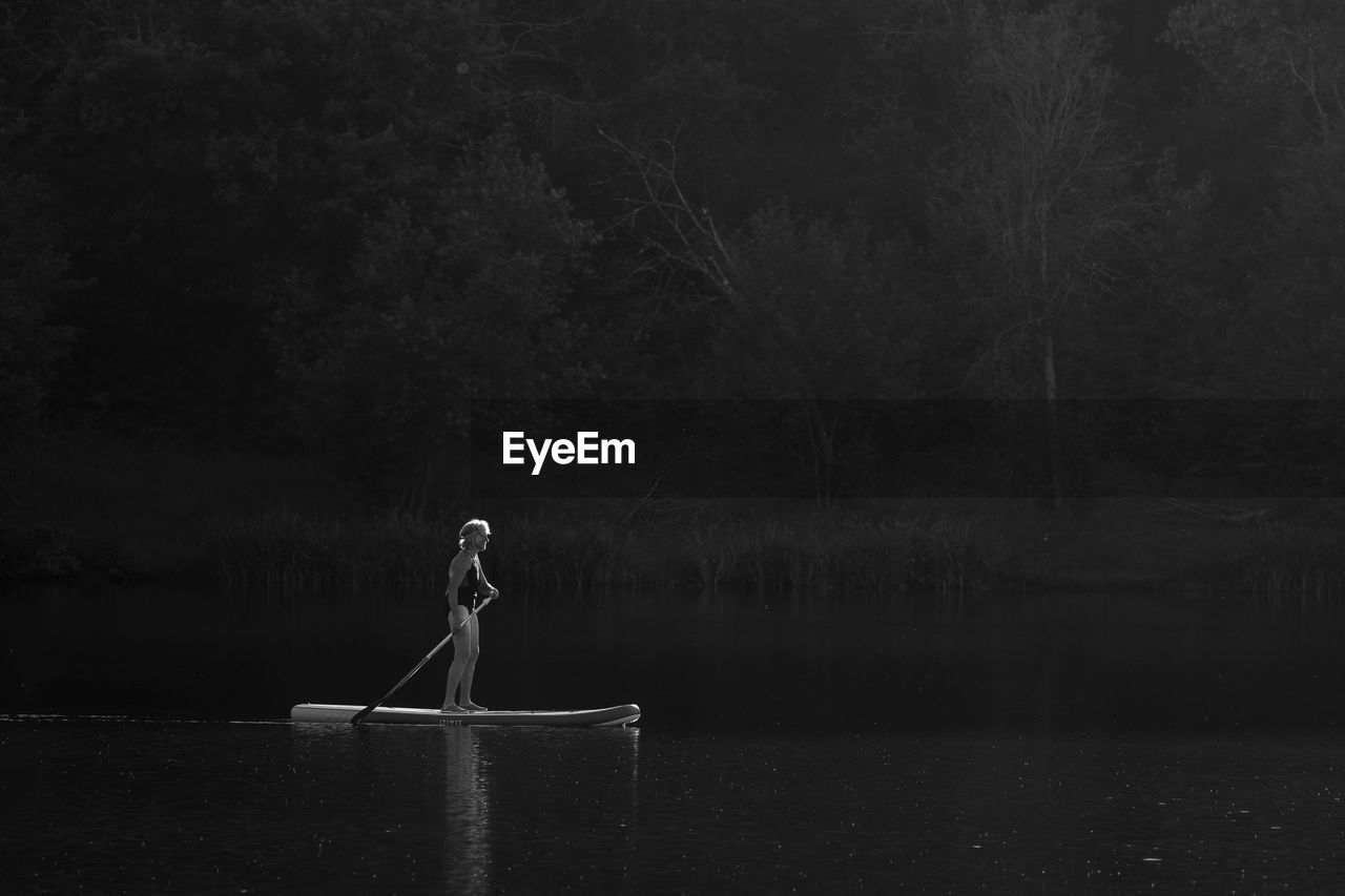 Elderly person paddleboarding on a lake alone at sunset