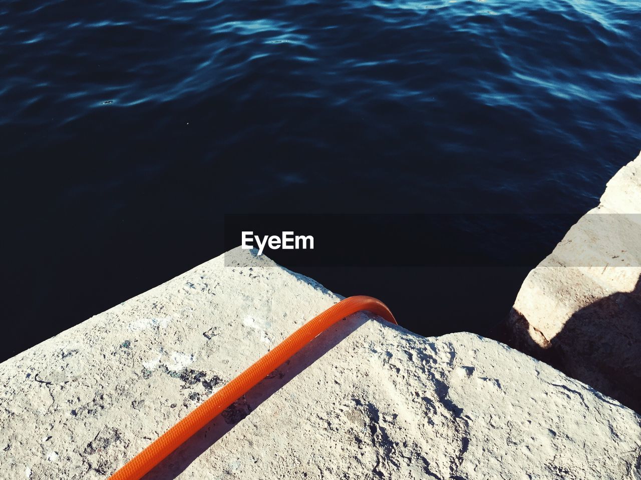 Close-up high angle view of an orange hose disappearing over a wall into the sea