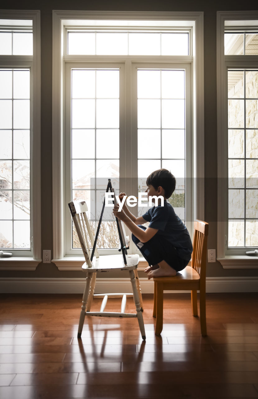 Young boy drawing on a canvas on an easel in front of windows.