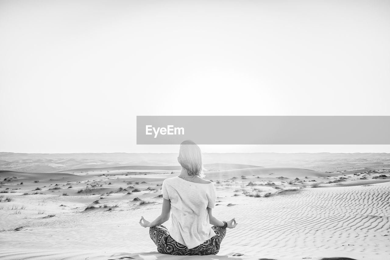 Rear view of woman meditating in desert