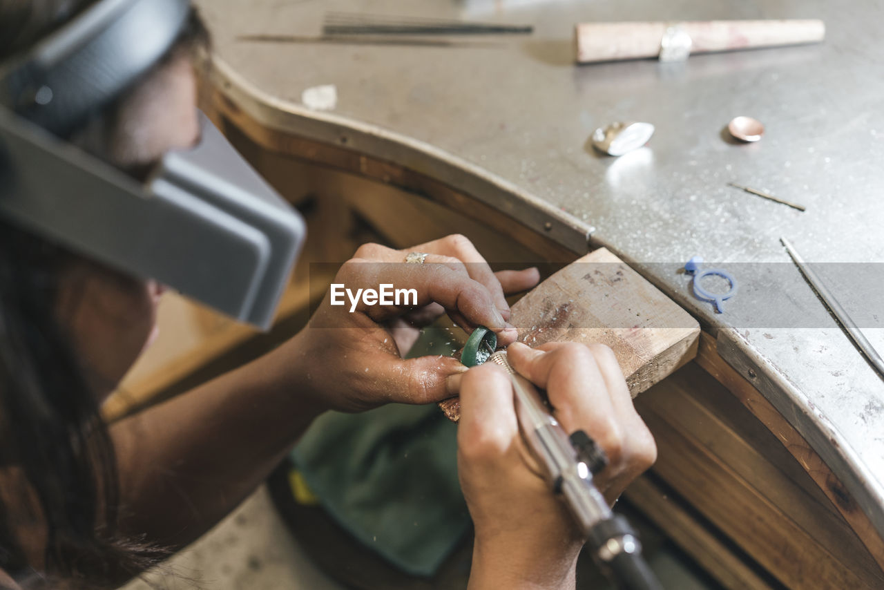 High angle view of female artisan shaping ring with equipment on table in workshop