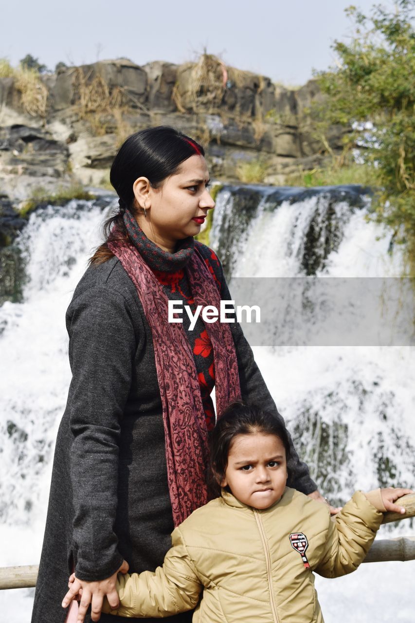 A young woman with her daughter standing near to a waterfall