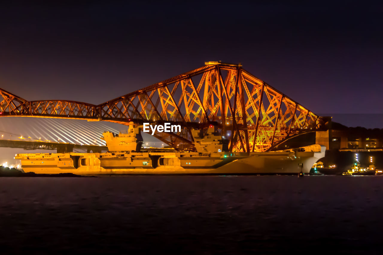 Illuminated bridge over sea against clear sky at night