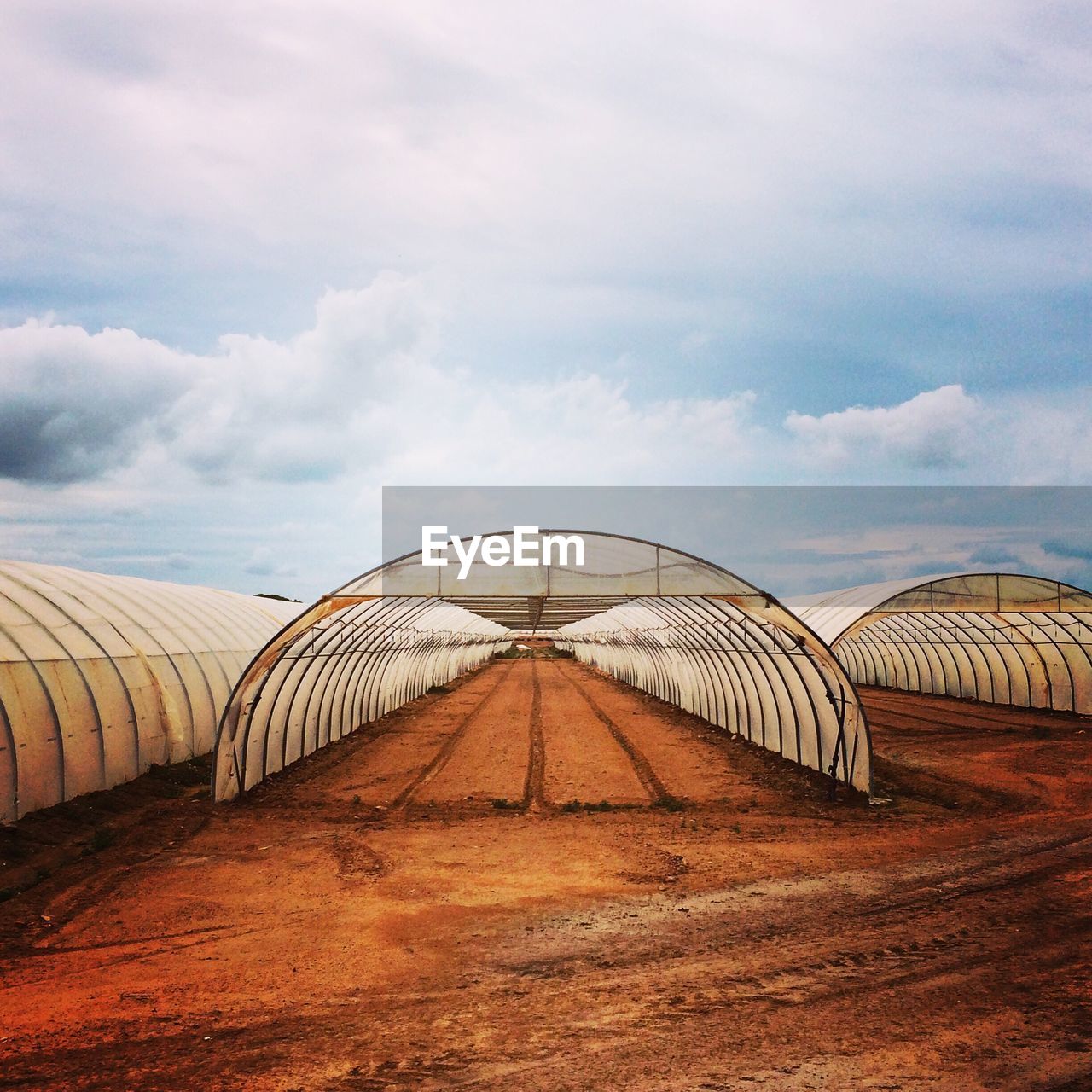 Empty greenhouses against cloudy sky