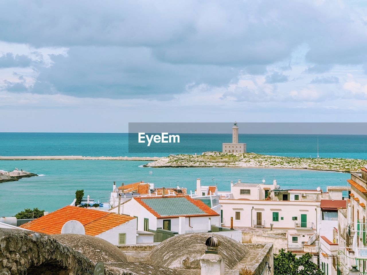 Lighthouse and buildings by sea against cloudy sky